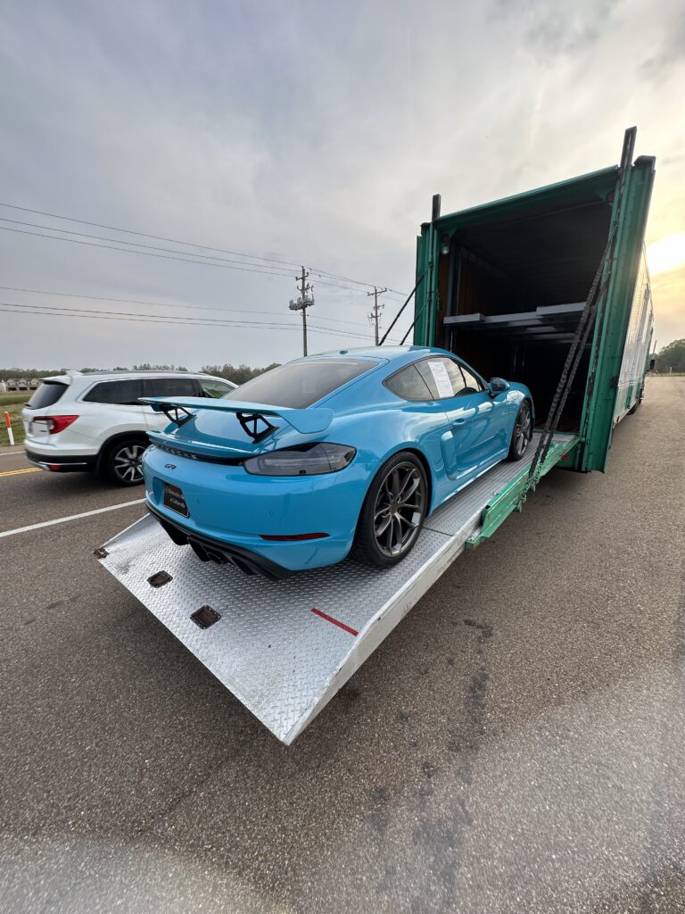 Porsche GT being loaded into the back of an enclosed auto trailer for transport.