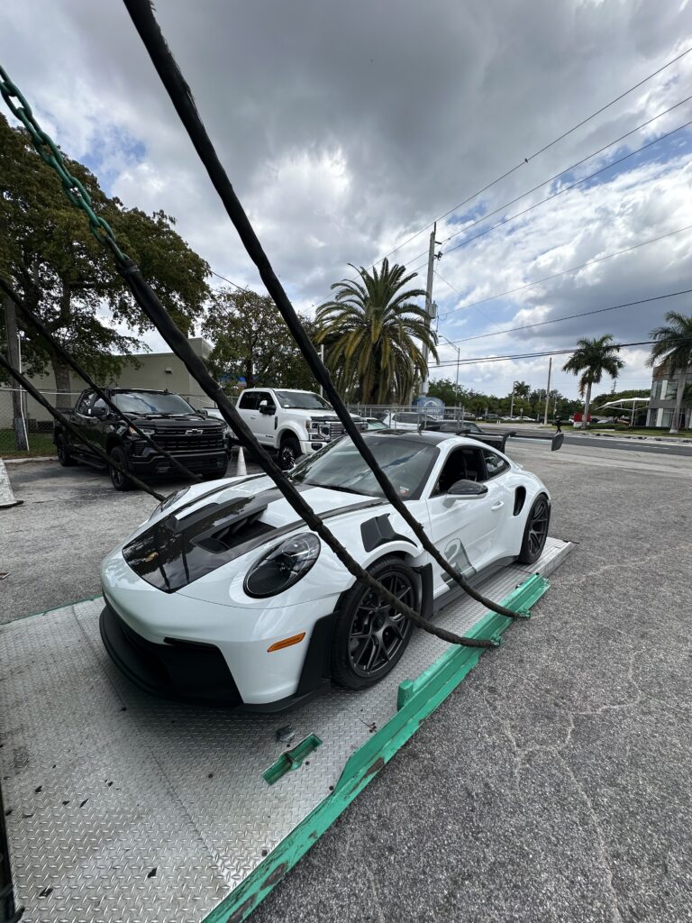 Porsche being carefully loaded into the back of an enclosed trailer to be transported.