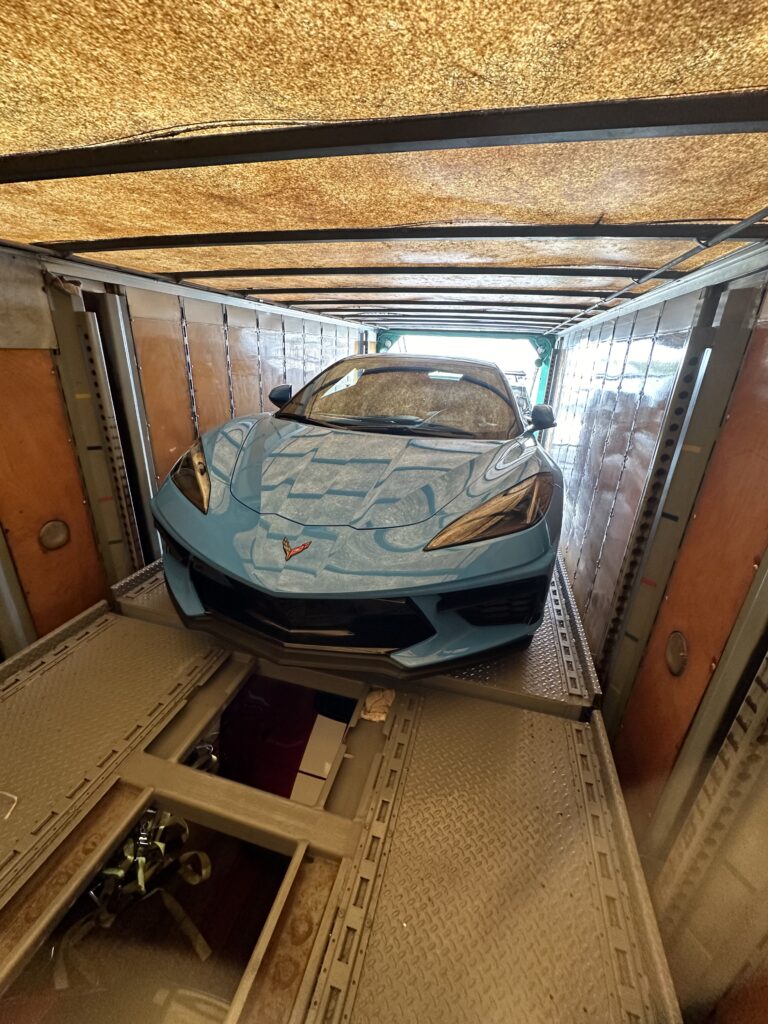 Corvette that has been carefully loaded into the back of an enclosed trailer that is ready for transport.