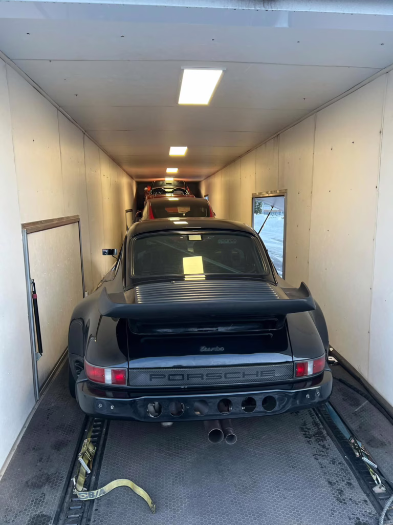 Black Porsche loaded in the back of an enclosed trailer.